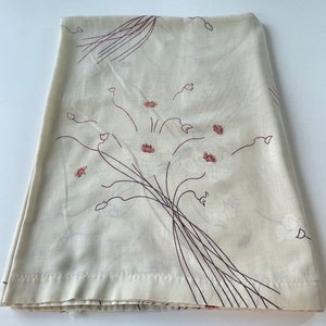 May include: Folded cream-colored fabric with a floral pattern. The design features brown stems and pink and white flower clusters. The fabric is folded neatly, showcasing the pattern's repeating design. The overall aesthetic is vintage and delicate.
