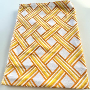 May include: A folded white and yellow patterned towel. The towel features a repeating geometric design of yellow and orange stripes, creating a woven effect. The towel is made of a soft, absorbent material, suitable for use in a bathroom or kitchen.