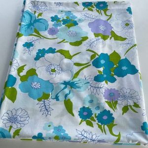 Könnte beinhalten: Weißer Stoff mit einem Blumenmuster mit großen türkisfarbenen, hellblauen und lavendelfarbenen Blumen mit grünen Blättern. Die Blumen haben weiße und türkisfarbene Zentren. Der Stoff ist gefaltet.