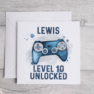 May include: A white card with blue watercolor splatters and a blue video game controller. The card says "Lewis Level 10 Unlocked".