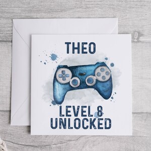 May include: A blue and white birthday card with a watercolor illustration of a video game controller. The card says "Theo Level 8 Unlocked".