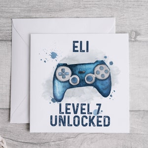 May include: A white card with blue watercolor splatters and a blue video game controller. The card says "Eli Level 7 Unlocked".