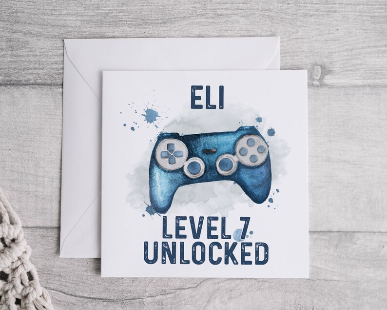 May include: A white card with blue watercolor splatters and a blue video game controller. The card says "Eli Level 7 Unlocked".