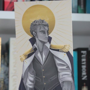 Puede incluir: Una ilustración en escala de grises de una persona que lleva una corona y un traje blanco y negro con detalles dorados. La persona está de pie frente a un sol dorado con rayos.