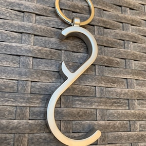 May include: Silver-toned keychain with a loop for attaching keys. The keychain has a hook-like design with a small black rubber tip at the end.