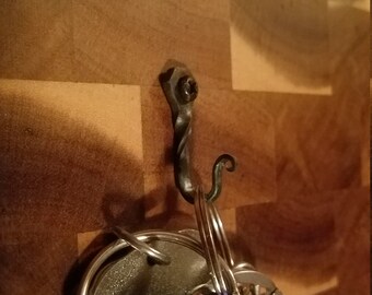 May include: A close-up of a metal hook screwed into a wooden surface. A set of keys is hanging from the hook.