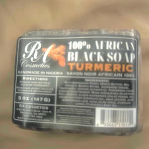 Puede incluir: Una pastilla envuelta de jabón negro africano 100% con cúrcuma. La etiqueta dice "RA Cosmetics" y "Hecho a mano en Nigeria". La pastilla pesa 147 gramos.