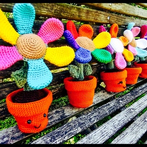May include: A row of six colorful crocheted flower pots with happy faces. Each pot is filled with a crocheted flower with different colored petals.