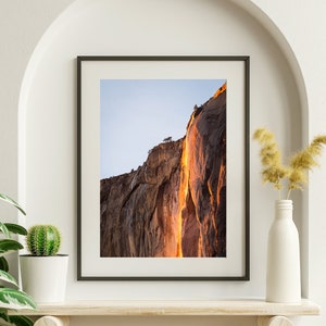 May include: A framed photograph of a waterfall cascading down a rocky cliff face. The water appears to be glowing orange and yellow, creating a dramatic and colorful scene.