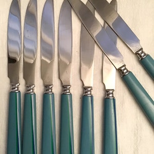 May include: Set of seven stainless steel knives with teal handles. The handles have a tapered design with a vertical stripe pattern in shades of green and blue. The blades are smooth and shiny, with a slight curve.
