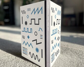 May include: A white journal with a black and blue geometric pattern on the cover. The text "MUSIC JOURNAL NOTES LYRICS IDEAS" is printed on the spine.