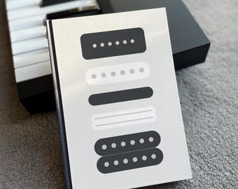 May include: A white notebook with black and white illustrations of guitar pickups. The notebook has a white background and black text.