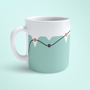 May include: A white ceramic mug with a teal green design featuring a black line with three red dots and a black circle. The mug has a white handle.