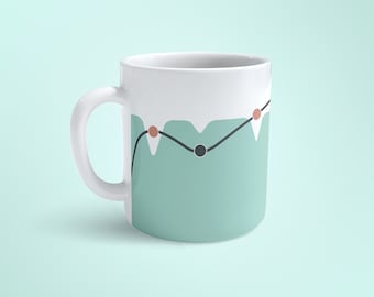 May include: A white ceramic mug with a teal green design featuring a black line with three red dots and a black circle. The mug has a white handle.