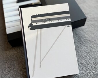 May include: A white card with a black and white illustration of a keyboard with a stand. The keyboard has a silver trim and a black and white design.