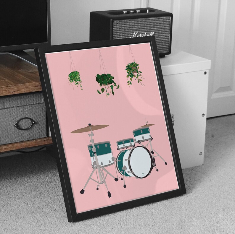 May include: A pink framed print with a black and white illustration of a drum set with three drums and a cymbal. The drums are green and white with a black rim. There are three hanging plants in the background.