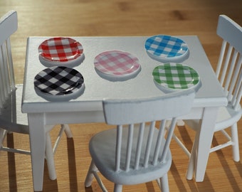 May include: A white table with four white chairs and five checkered plates in different colors. The plates are red and white, black and white, pink and white, blue and white, and green and white.