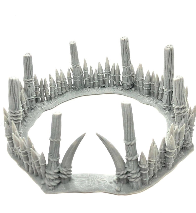 May include: A gray plastic model of a circular fence with pointed stakes and wooden posts. The fence is made to look like it is made of wood and rope.