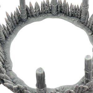 May include: A gray plastic model of a circular wooden fence with pointed stakes. The fence is made of several wooden posts and a row of pointed stakes around the top.