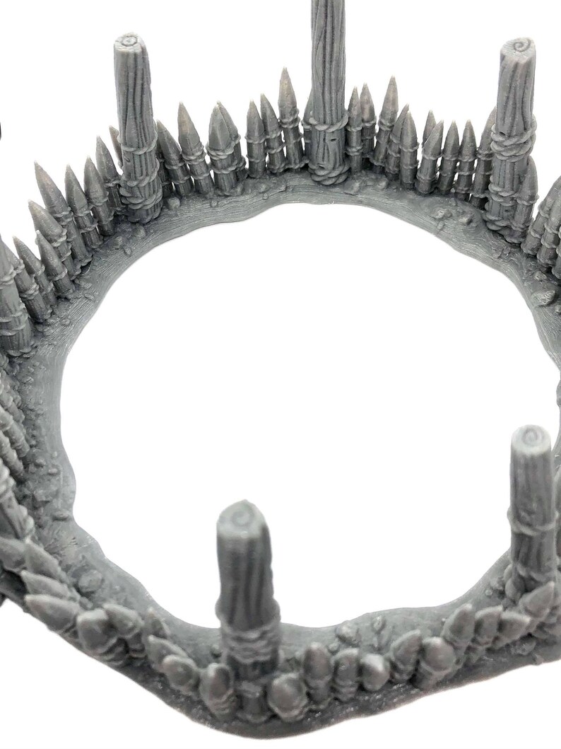 May include: A gray plastic model of a circular wooden fence with pointed stakes. The fence is made of several wooden posts and a row of pointed stakes around the top.