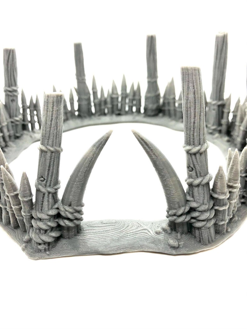 May include: A gray 3D printed crown with a wooden base and two large horns. The crown is decorated with rope and spikes.