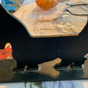May include: Black metal silhouette of a Scottish Terrier dog mounted on a black metal base. The dog is standing on all four legs with its tail curled up. The base has two holes on the top and two holes on the bottom.