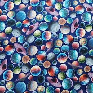 Peut inclure: Un tissu bleu avec un motif répété de planètes et de lunes colorées. Les planètes ont des anneaux et sont dans différentes nuances de bleu, vert, orange et rouge.