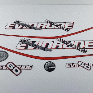Op de afbeelding: Een set zwarte en witte Evinrude-bootmotor stickers met rode accenten. De stickers bevatten het Evinrude-logo, de woorden "Saltwater Series" en het nummer "60". Er is ook een zwart-wit BRP-logo.