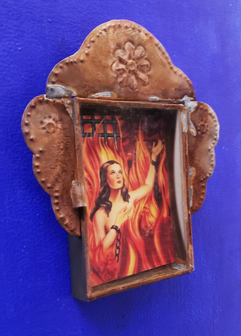 May include: A framed image of a woman in a fiery setting, with a rusted metal frame featuring a decorative flower design.