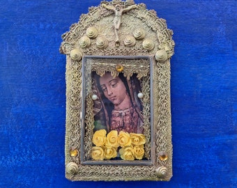 Könnte beinhalten: Ein verzierter goldfarbener Rahmen mit einem religiösen Bild einer Frau mit Dornenkrone und Blumen. Der Rahmen ist mit goldenen Perlen und Spitze verziert.