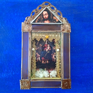 May include: A small, ornate, wooden frame with a glass front, containing a religious image of the Virgin Mary and baby Jesus. The frame is decorated with gold trim and has a blue background.