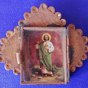 May include: A small, hinged, metal frame with a scalloped edge. The frame contains a printed image of a man in a green robe holding a staff. The image is set against a red background.
