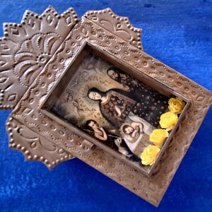 May include: A silver-toned metal frame with an ornate design, featuring a vintage photograph of a family inside. The frame is decorated with yellow paper flowers.