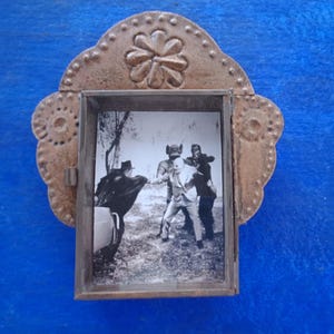 May include: A vintage-style metal picture frame with a decorative floral design. The frame holds a black and white photograph of three people standing in a field.
