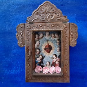 May include: A small, ornate wooden frame with a glass front, depicting a religious image of a heart with thorns and surrounded by angels. The frame is decorated with metal accents and has a blue background.