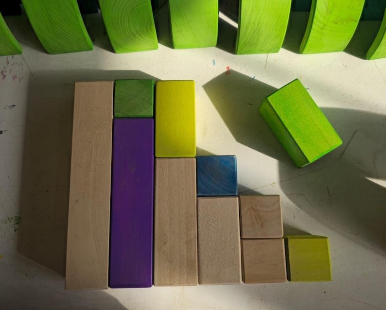 May include: A collection of colorful wooden blocks in various shapes and sizes. The blocks are arranged in a visually appealing pattern, with a mix of natural wood, green, purple, yellow, and blue hues. The image is well-lit, highlighting the textures and colors of the blocks.