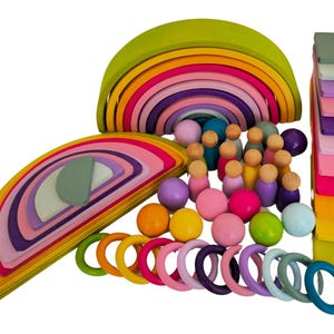 May include: A wooden toy set featuring two large nested rainbow arches in shades of green, yellow, orange, pink, and purple. The set includes small wooden peg dolls, colorful spheres, rings, and a stack of rectangular blocks in various pastel colors.