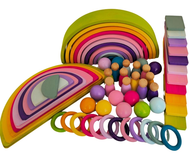 May include: A wooden toy set featuring two large nested rainbow arches in shades of green, yellow, orange, pink, and purple. The set includes small wooden peg dolls, colorful spheres, rings, and a stack of rectangular blocks in various pastel colors.