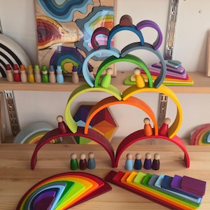 May include: A collection of wooden rainbow stacking arches and small peg dolls in various colors. The arches are arranged in a tiered structure, with several peg dolls placed on top of the curves and others standing on the surface below.
