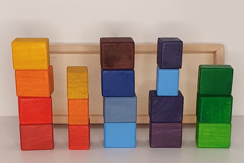 May include: A set of colorful wooden blocks stacked in different heights. The blocks are painted in shades of yellow, orange, red, brown, blue, green, and purple.