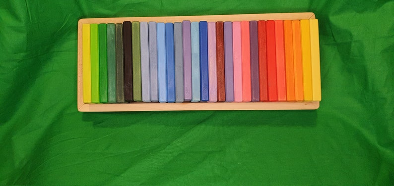 May include: A wooden box filled with colorful wooden blocks. The blocks are arranged in a rainbow pattern, with each block a different shade of color.