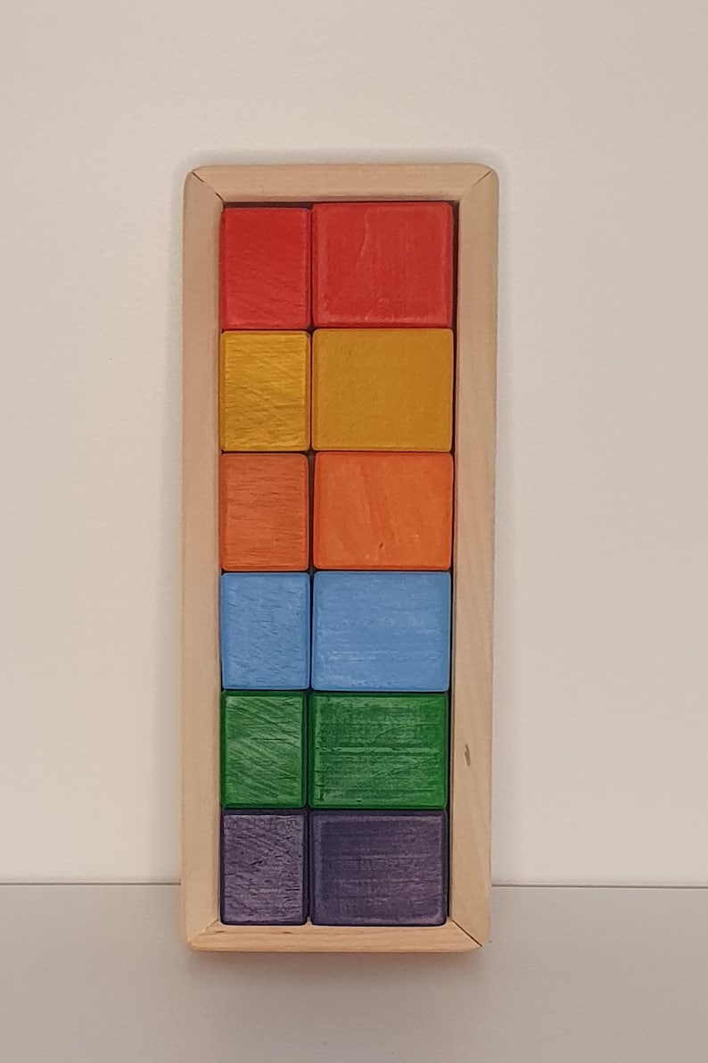 May include: A wooden box with a rainbow of colored blocks inside. The blocks are arranged in rows of two, with each row a different color. The colors are red, orange, yellow, green, blue, and purple.