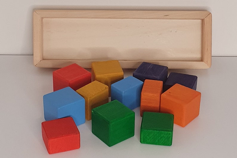 May include: A set of 10 wooden blocks in various colors, including red, orange, yellow, green, blue, and purple. The blocks are arranged in a semi-circle on a white surface.