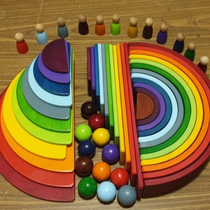 May include: A rainbow-colored wooden arch with 12 pieces, each a different size and color. The arch is made of natural wood and has a smooth finish. There are 12 small wooden people surrounding the arch.