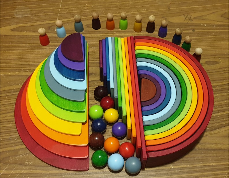 May include: A rainbow-colored wooden arch with 12 pieces, each a different size and color. The arch is made of natural wood and has a smooth finish. There are 12 small wooden people surrounding the arch.