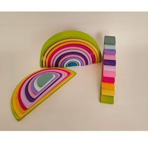 May include: A set of wooden stacking toys featuring two arched rainbow structures and a vertical tower of rectangular blocks. The pieces are painted in a spectrum of colors including lime green, yellow, orange, pink, purple, and light blue.