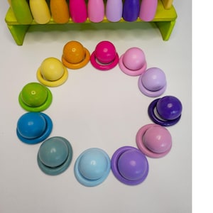 May include: A set of wooden peg dolls in various colors arranged in a row on a yellow tiered stand, with matching wooden balls and rings arranged in a circular pattern below. The colors include shades of green, yellow, orange, pink, purple, and blue.