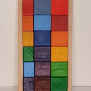 May include: A wooden box with a rainbow of colored blocks inside. The blocks are arranged in a grid pattern, with each row containing a different color.