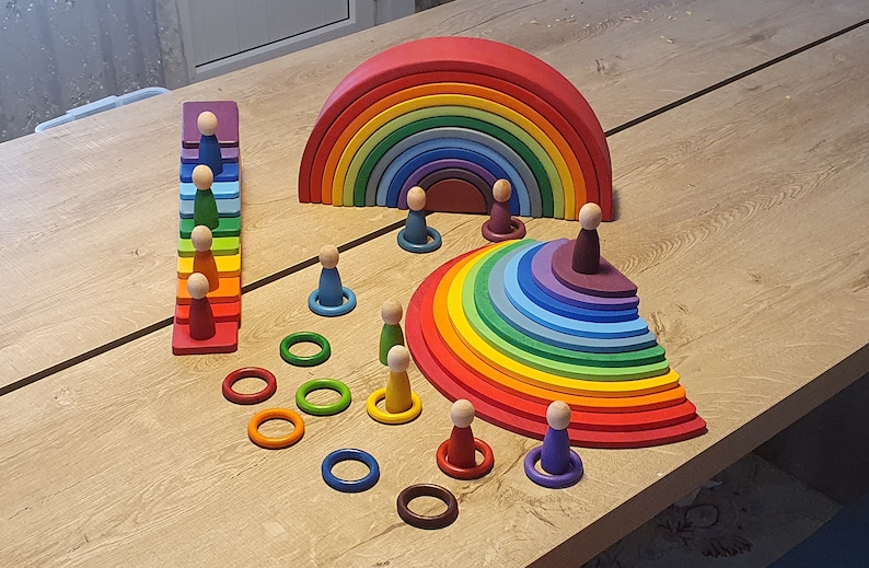 May include: A rainbow wooden arch, a rainbow wooden half-circle, a rainbow wooden staircase, and a set of wooden rings and figures. The toys are made of natural wood and painted in bright colors.