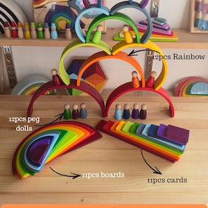 May include: A 46-piece wooden toy set featuring a 12-piece rainbow arch stacker, 12 peg dolls, 11 boards, and 11 cards. The items are painted in various colors including red, orange, yellow, green, blue, and purple. Text labels identify the components as 12pcs Rainbow, 12pcs peg dolls, 11pcs boards, 11pcs cards, and 46 pcs Set.